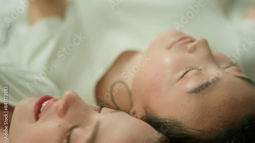 Wallpaper Mural Two multiracial friends multiethnic women diversity girls female Caucasian woman Asian Korean Japanese Chinese girl relaxing together lying on bed closed eyes listening music in wired headphones audio Torontodigital.ca