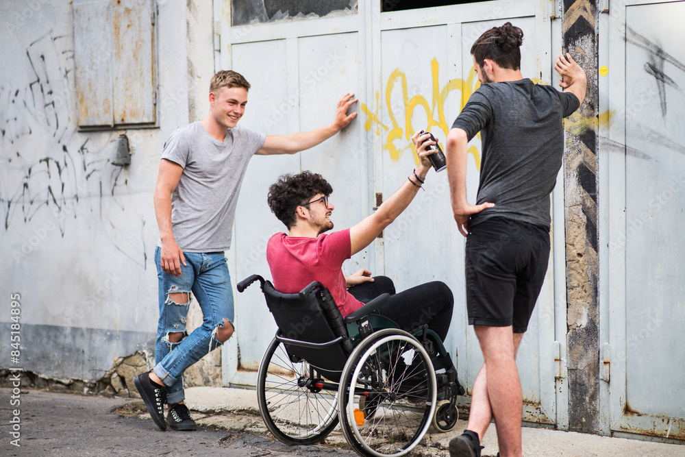 Young man in wheelchair spending free time outdoor with friends, having fun in city. Male friendship. Young man in wheelchair spending free time outdoor with friends, having fun in city. Male friendship.