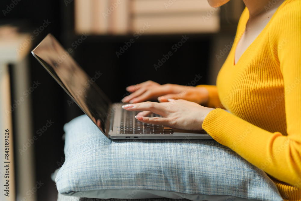 Naklejka premium Cozy Work from Home: Woman in Yellow Sweater Using Laptop on a Pillow