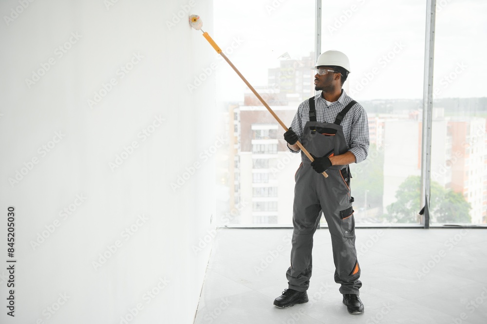 African man in a helmet paints a white piece of wall with paint African man in a helmet paints a white piece of wall with paint