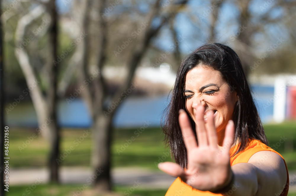 Pretty young woman, brunette and orange dress puts her hand in front of her face to protect herself. The girl smiles and feels ashamed. Spotlight on her face. Pretty young woman, brunette and orange dress puts her hand in front of her face to protect herself. The girl smiles and feels ashamed. Spotlight on her face.