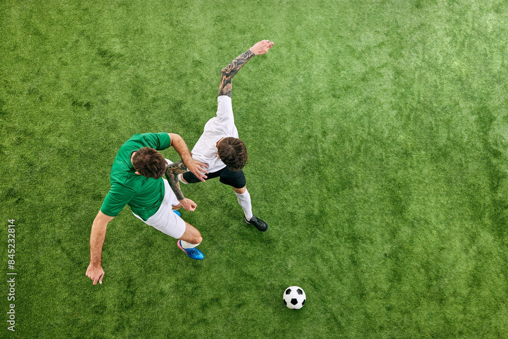 Fototapeta premium Aerial view. Dynamic photo of young football athletes in different uniform playing game on green lush playground. Concept of professional sport, championship, final match, movement. Ad