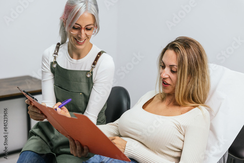 Microblading technician discusses the process with a smiling client seated in a salon photo