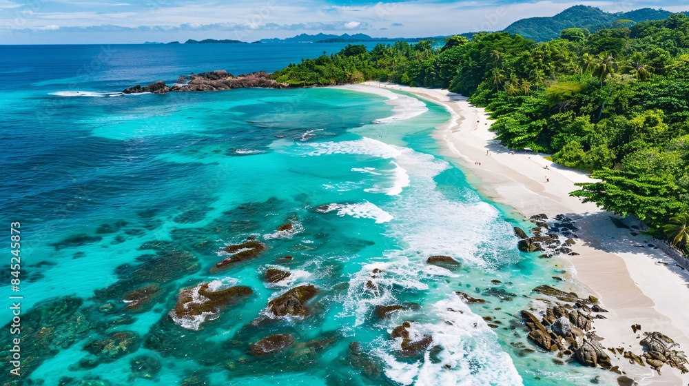 Obraz premium A breathtaking aerial top view of an idyllic white sand beach surrounded by lush green forests and crystal-clear turquoise waters, with gentle waves crashing against rocky outcrops, creating a serene