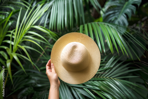 Summer vacations concept, woman hand with straw hat in front of green tropical leaves. Tropical islands vacation. photo