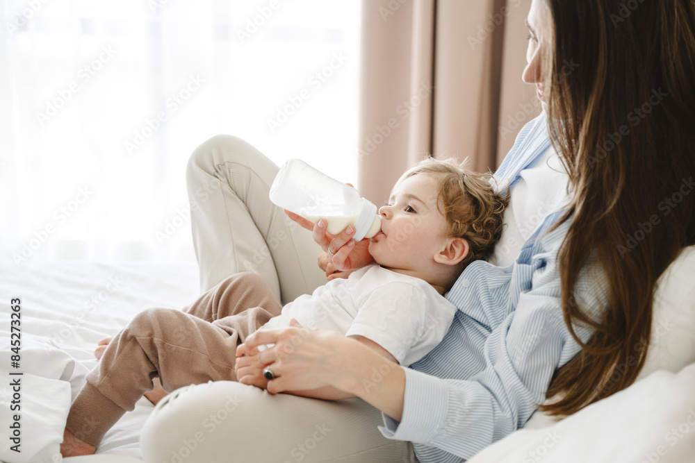 Mother feeding milk through bottle to baby son at home Mother feeding milk through bottle to baby son at home