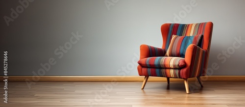 A square striped armchair with a fringed throw pillow is placed inside a living room with a wooden floor The setting provides a copy space image