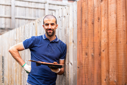 Smiling man leaning with paint tray on fence in back yard photo