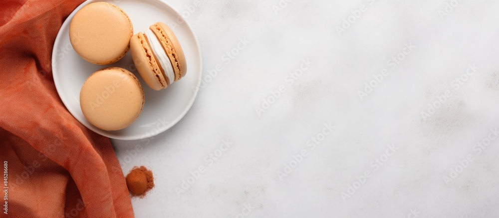A top down view of orange macarons or macaroon cakes on a white concrete surface with a cup of coffee nearby The image includes linen textile and ample space for text A top down view of orange macarons or macaroon cakes on a white concrete surface with a cup of coffee nearby The image includes linen textile and ample space for text