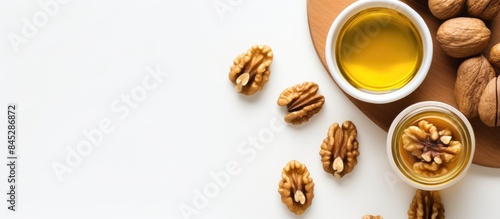 A top down view of a jar of walnut oil placed near a bowl of walnuts on a white background offering copy space for various purposes such as skin care or cooking