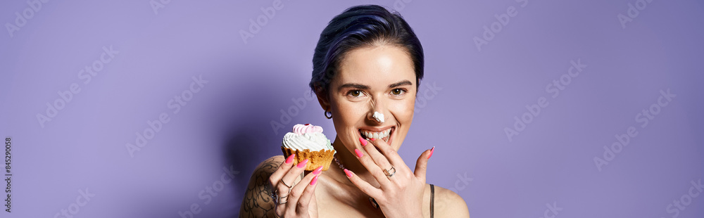 A pretty young woman with short blue hair in a silver party dress hides her face behind a delicious cupcake. A pretty young woman with short blue hair in a silver party dress hides her face behind a delicious cupcake.
