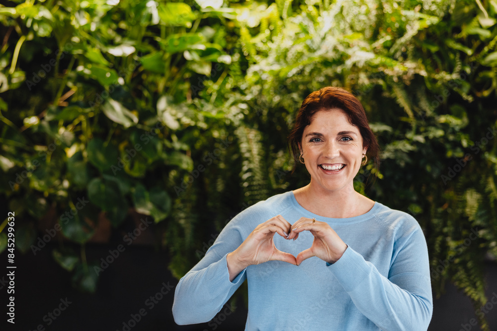 Happy business woman showing a heart gesture while standing in a green office Happy business woman showing a heart gesture while standing in a green office