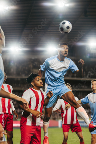 Intense football match with players going for a header at a night stadium