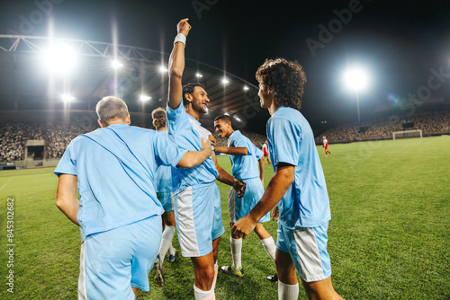 Professional football players celebrating victory at a stadium match under bright lights photo