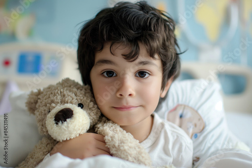 Dark-haired boy in a hospital bed hugging a teddy bear, looking happy and confident, surrounded by a cozy and softly lit bedroom