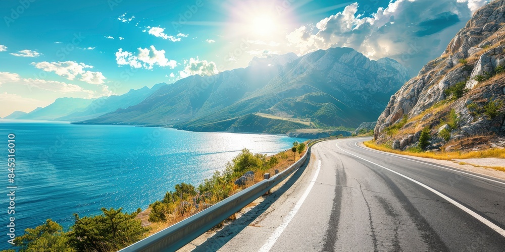 Obraz premium Empty highway on the background of steep mountain peaks, sea coast on one side of the road, blue water, clear sunny day