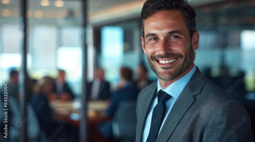 A businessman standing at the entrance to a boardroom with a group of coworkers meeting in the background A businessman standing at the entrance to a boardroom with a group of coworkers meeting in the background