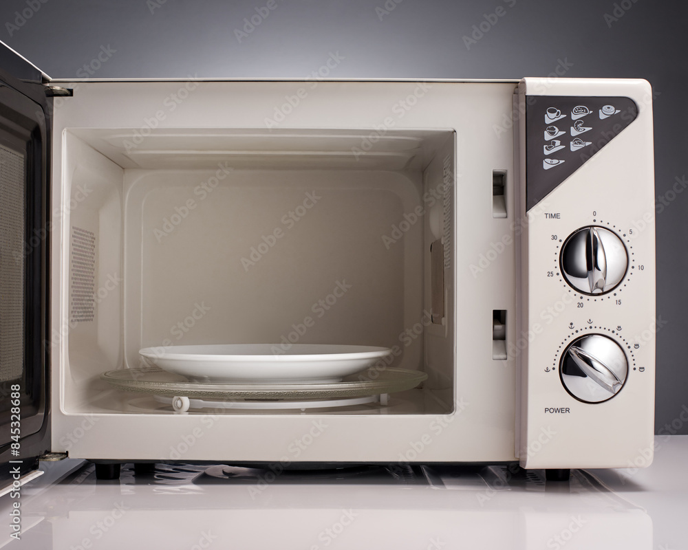 Obraz premium White open microwave with plate on gray background