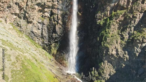 Smooth flight in the mountains above the waterfall. A powerful stream breaks down. Rainbow rays in the waterfall. Altay.