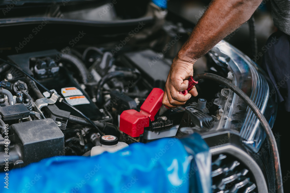 Closeup mechanic worker hand clamping car battery terminal for jump start low voltage battery vehicle in garage. Closeup mechanic worker hand clamping car battery terminal for jump start low voltage battery vehicle in garage.