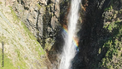 Smooth flight in the mountains above the waterfall. A powerful stream breaks down. Rainbow rays in the waterfall. Altay.