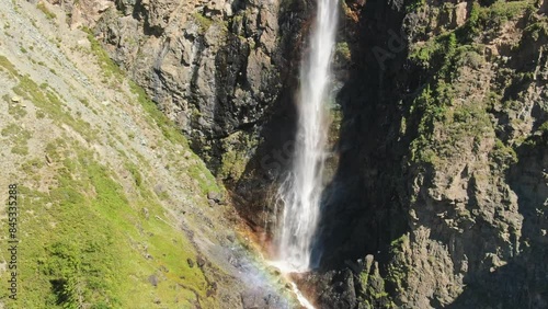 Smooth flight in the mountains above the waterfall. A powerful stream breaks down. Rainbow rays in the waterfall. Altay.