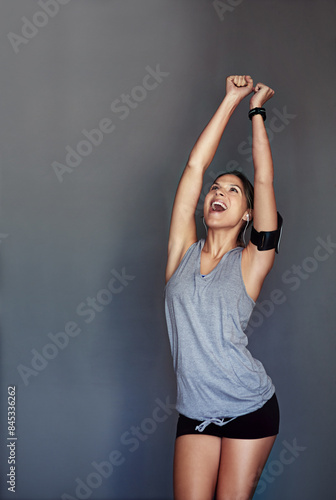 Excited woman, fitness and celebration with fist pump for winning, success or goals on a gray studio background. Happy female person, athlete or winner with smile for victory, achievement or results © peopleimages.com