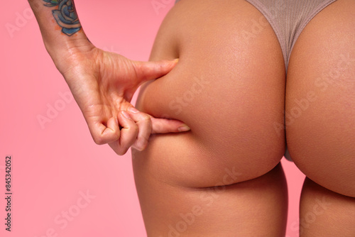 A closeup image captures the texture of skin on a tattooed hand pinching a thigh