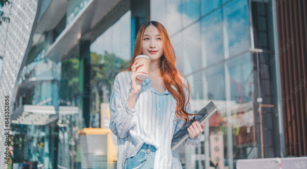 Fototapeta premium A woman with red hair is holding a cup of coffee and a laptop