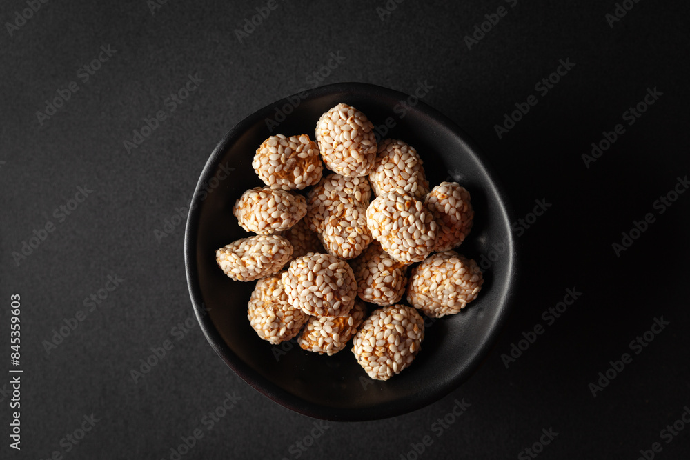Top view of a black bowl filled with Indian sweet item called 'Rewri' or 'Revdi' or Sesame seeds sweet, on a black background. Top view of a black bowl filled with Indian sweet item called 'Rewri' or 'Revdi' or Sesame seeds sweet, on a black background.