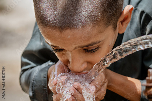 A thirsty Pakistani boy drinking water from a water supply tap on a hot day