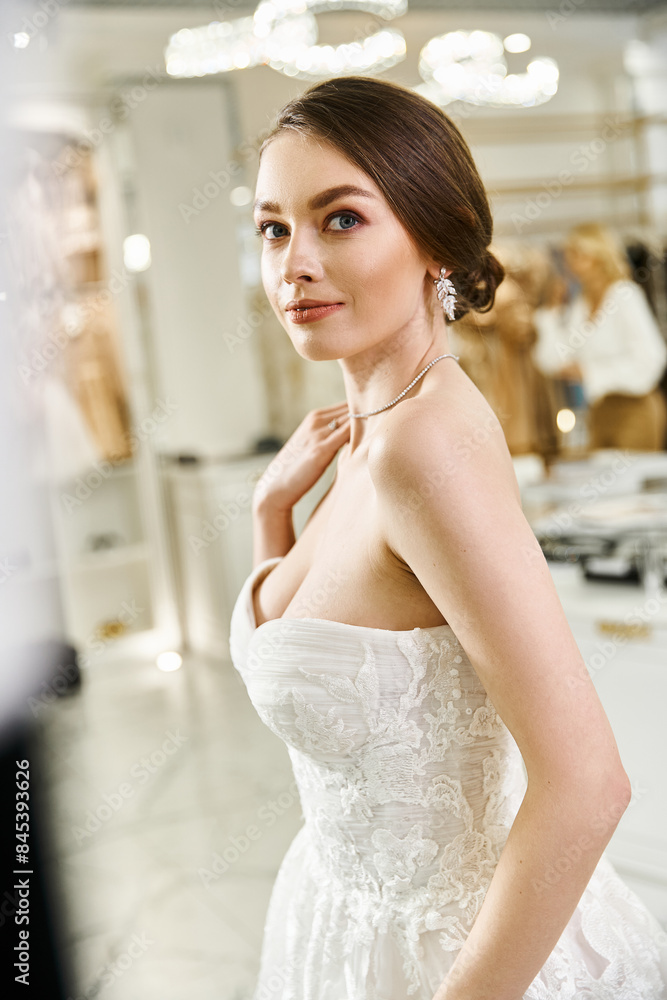 Naklejka premium A young brunette bride in a white wedding dress strikes a pose for a picture in a wedding salon.