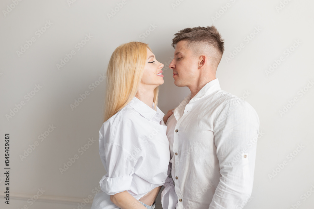 fashion beautiful young couple of lovers in a fashionable white shirt stands near a white wall and is ready to kiss fashion beautiful young couple of lovers in a fashionable white shirt stands near a white wall and is ready to kiss