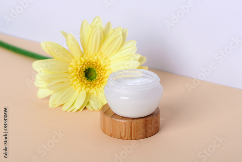 Cosmetic cream jar and yellow gerbera flowers on neutral background. Closeup