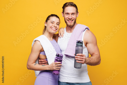 Fototapeta Naklejka Na Ścianę i Meble -  Young happy strong fitness trainer instructor sporty two man woman wear blue clothes spend time in home gym hold bottle of water, towel isolated on plain yellow background. Workout sport fit concept.