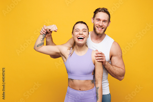 Young cool strong fitness trainer instructor sporty two man woman wear blue clothes spend time in home gym showing biceps muscles on hand isolated on plain yellow background Workout sport fit concept photo