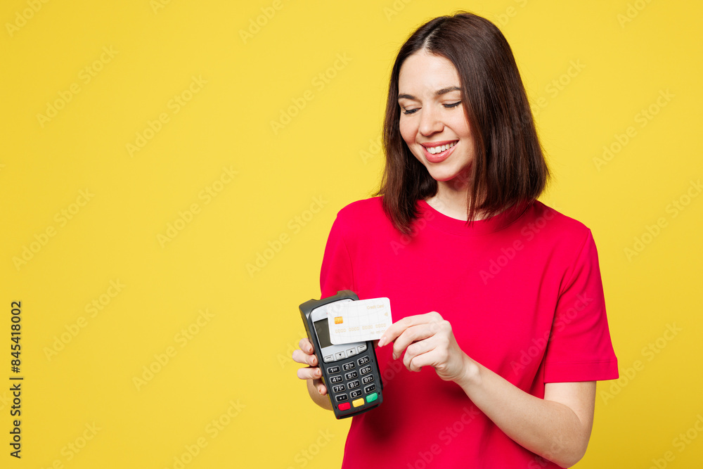 Young woman wear pink t-shirt casual clothes hold wireless modern bank payment terminal to process acquire credit card isolated on plain yellow orange background studio portrait. Lifestyle concept. Young woman wear pink t-shirt casual clothes hold wireless modern bank payment terminal to process acquire credit card isolated on plain yellow orange background studio portrait. Lifestyle concept.