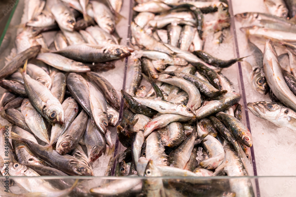 This image shows a variety of fresh fish laid out on ice presumably at a seafood market, with blurred faces behind the stall This image shows a variety of fresh fish laid out on ice presumably at a seafood market, with blurred faces behind the stall