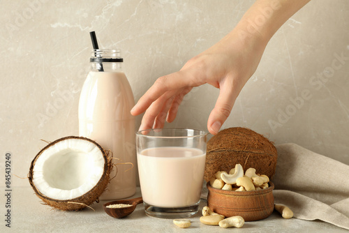 Bottle and glass of milk, hand, coconut and nuts on beige background