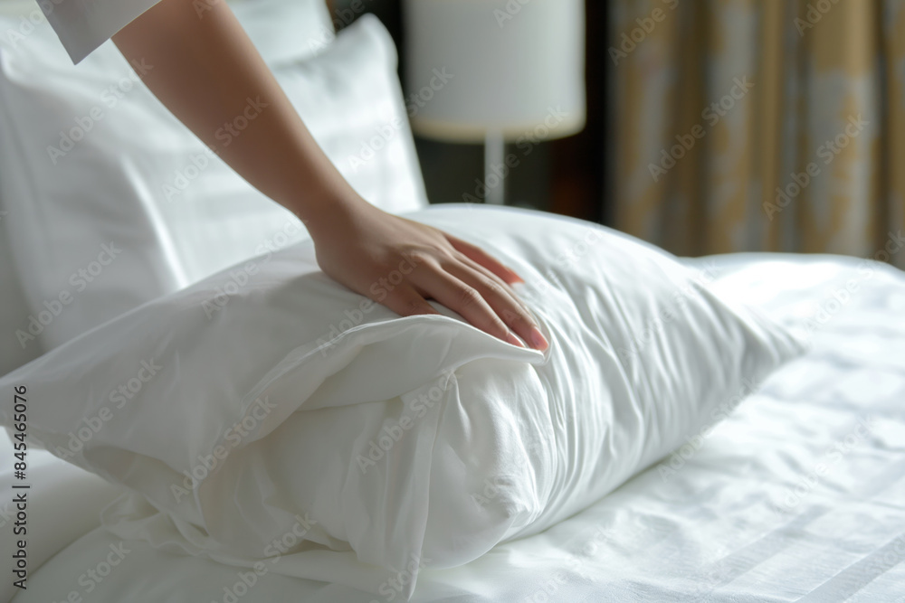 A person adjusting a pillow on a hotel bed to ensure comfort and neatness in the room A person adjusting a pillow on a hotel bed to ensure comfort and neatness in the room