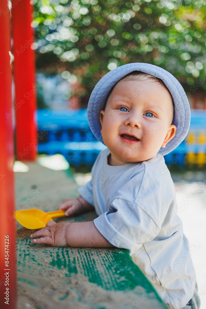 A little baby boy, 11 months old, in a t-shirt and a panama on his head, plays with sand on a summer day. A child is playing on the street. A little baby boy, 11 months old, in a t-shirt and a panama on his head, plays with sand on a summer day. A child is playing on the street.