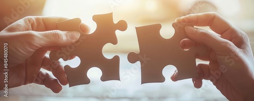 Hands fitting two large jigsaw puzzle pieces together against a warm, glowing background, symbolizing problemsolving or partnership photo