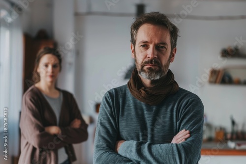 Portrait of a bearded man standing with his arms crossed in front of his female colleague © Iigo