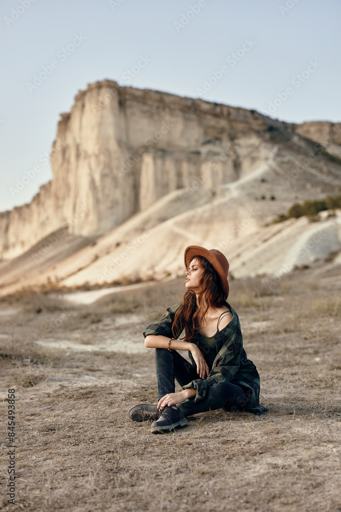 Woman wearing hat sits in front of mountain, admiring scenic view on sunny day Woman wearing hat sits in front of mountain, admiring scenic view on sunny day