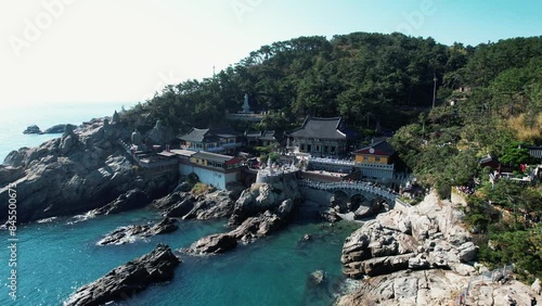 aerial view of the Haedong Yonggungsa Temple in Busan, Korea, majestically perched on rocky cliffs above the sea, surrounded by lush greenery under clear skies. photo