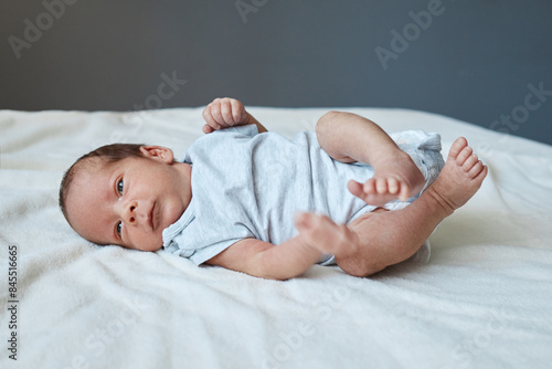 Infancy, healthcare and pediatrics, growth. Close up view of cutie newborn wearing bodysuit lying alone on bed adorable baby resting on bedsheets moving playing © sementsova321