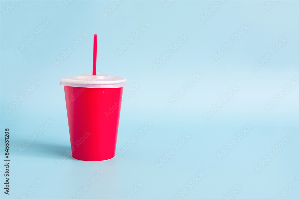 A red paper disposable cup with a red tube on a light background. A red paper disposable cup with a red tube on a light background.