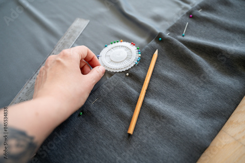 Hand holding Sewing pins are lying in case on fabric being hemmed. Image captures sewing process, emphasizing tools and precision required for hemming fabric