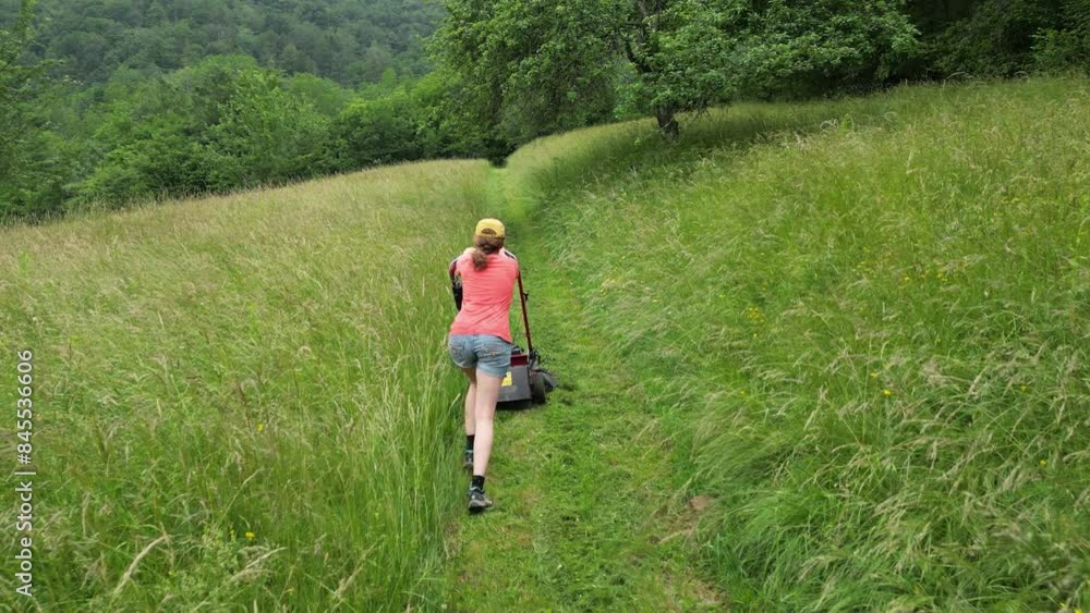 Drone View of Caucasian Adult Female Farmer mows a path across the lawn with a motorized lawnmower - Slovenia Drone View of Caucasian Adult Female Farmer mows a path across the lawn with a motorized lawnmower - Slovenia