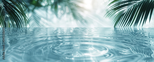 A serene image featuring still, blue water with a soft, rippling effect. The water is surrounded by the silhouette of palm tree leaves, creating a tranquil and peaceful atmosphere.